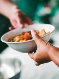 A volunteer handing a bowl of hot food across a serving table.