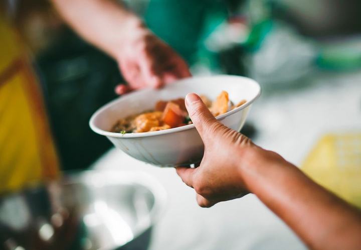 A volunteer handing a bowl of hot food across a serving table.