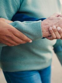 A hand steadying an older adult who is walking with a cane.